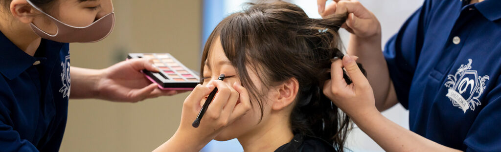 美容の授業で、生徒同士がヘアアレンジやメイクを実習している様子